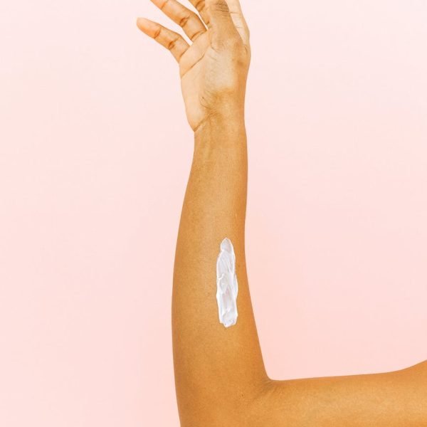 female arm with smear for skin care against pink background